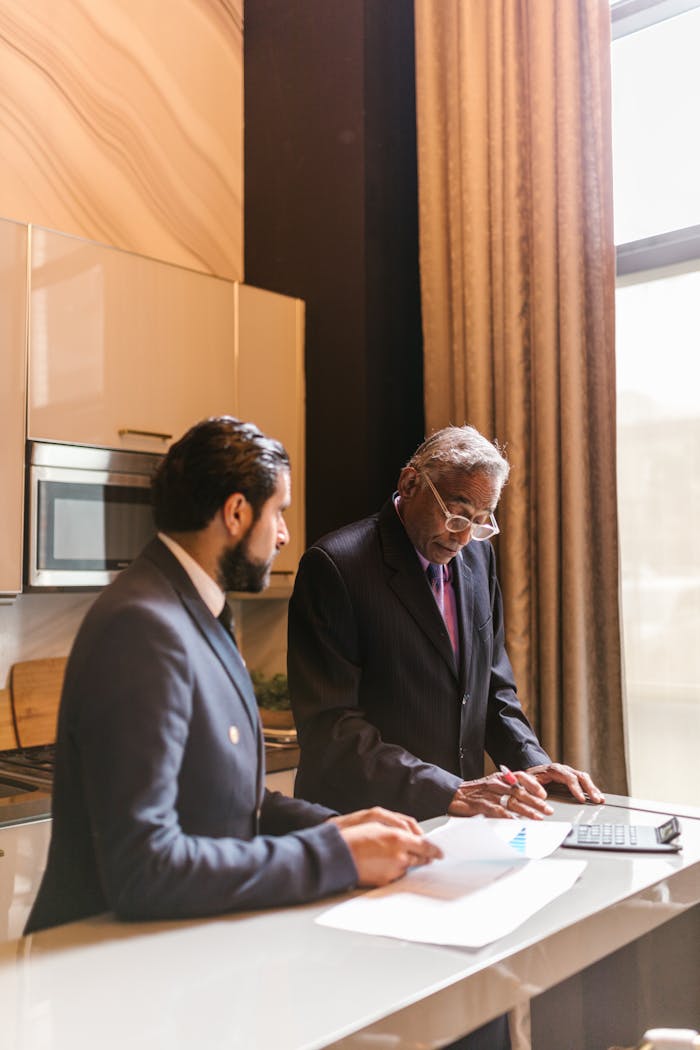 Two businessmen in suits collaborating over documents in a contemporary office setting.